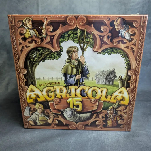 Die Agricola 15 Jahre Jubiläumsbox von Lookout Spiele zeigt einen verschnörkelten Holzrahmen, einen eine Mistgabel haltenden Bauern, ein Schaf, ein Haus im Hintergrund und illustrierte Figuren in jeder Ecke.
