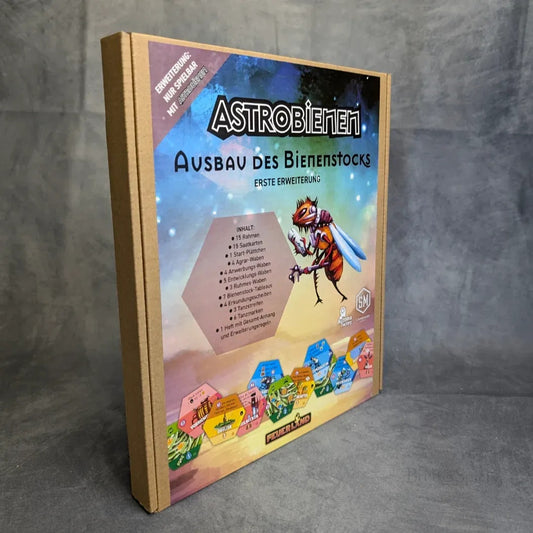 Die Schachtel des Brettspiels Astrobienen - Ausbau des Bienenstocks von Feuerland Spiele zeigt auf dem Cover eine gepanzerte Cartoon-Biene, sechseckige Spielsteine und den Spielinhalt vor einem grauen Hintergrund.