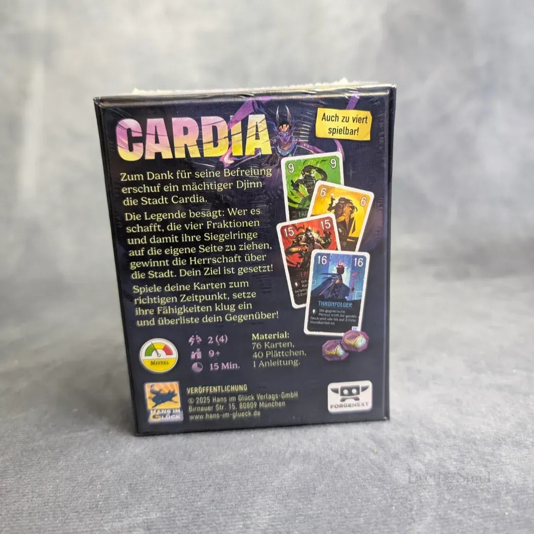 Eine Schachtel für Hans im Glück's Duell um Cardia steht auf einer grauen Fläche. Auf der Rückseite befinden sich bunte Karten, Spieldetails und ein deutscher Text zu diesem strategischen Duellspiel. Ein gelbes Etikett oben rechts verkündet: "Auch zu viert spielbar!.