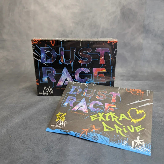 Zwei Dust Race inkl. Extra Drive Promo-Boxen von MM-Spiele stehen auf einer grauen Oberfläche: Eine steht aufrecht hinten, während die Extra Drive-Box flach vorne liegt, mit Graffiti-Artwork versehen ist und den hohen Wiederspielwert und die Fahrer-Kombination hervorhebt.