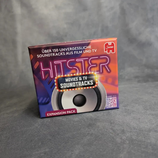 Eine Schachtel von Jumbo Spiele's Hitster: Movies & TV Soundtracks Erweiterungspaket mit buntem Neontext und einer Lautsprechergrafik auf grauem Hintergrund. Dieses Spiel enthält über 150 unvergessliche Film- und TV-Soundtracks.