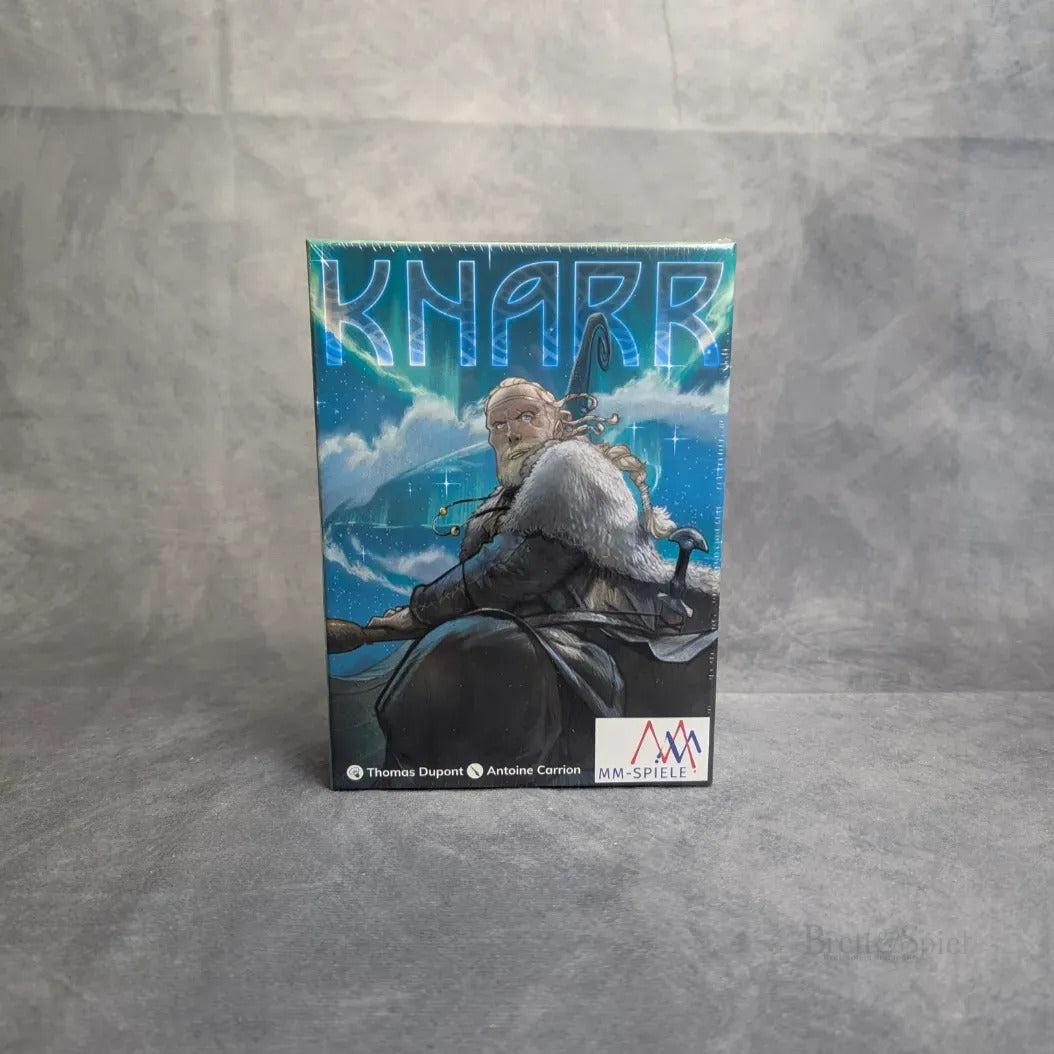 Eine Box-Ausgabe von „Knarr“ von MM-Spiele mit Wikinger-Motiven, darunter ein Anführer mit einem Ruder und seine Mannschaft vor einem Schiff auf Meereswellen, alles vor einem grauen Hintergrund.