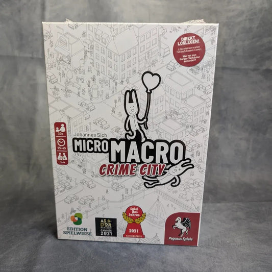 Das Bild zeigt die Schachtel von MicroMacro: Crime City das ultimative Bundle von Pegasus Spiele, mit einer schwarz-weißen Cartoon-Stadtszene und Symbolen für Auszeichnungen und Altersfreigabe am unteren Rand.