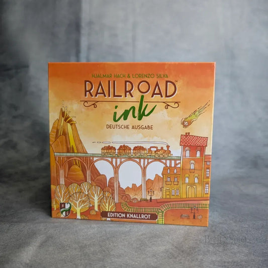 Die Abbildung zeigt die Schachtel für Railroad Ink: Edition Knallrot von Heidelbär Spiele. Das gelb-orangefarbene Cover zeigt Züge, Schienen, Gebäude, Bäume, einen Meteor und einen deutschen Text, der die Herausforderungen des Verkehrsnetzes hervorhebt.