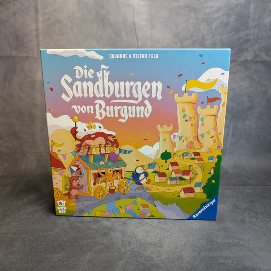 Die Box Die Sandburgen von Burgund von Ravensburger Spiele zeigt bunte Cartoon-Burgen, Tiere in einer Kutsche, Konfetti und ein festliches mittelalterliches Dorf. Die Designer Susanne & Stefan Feld sind oben aufgeführt.
