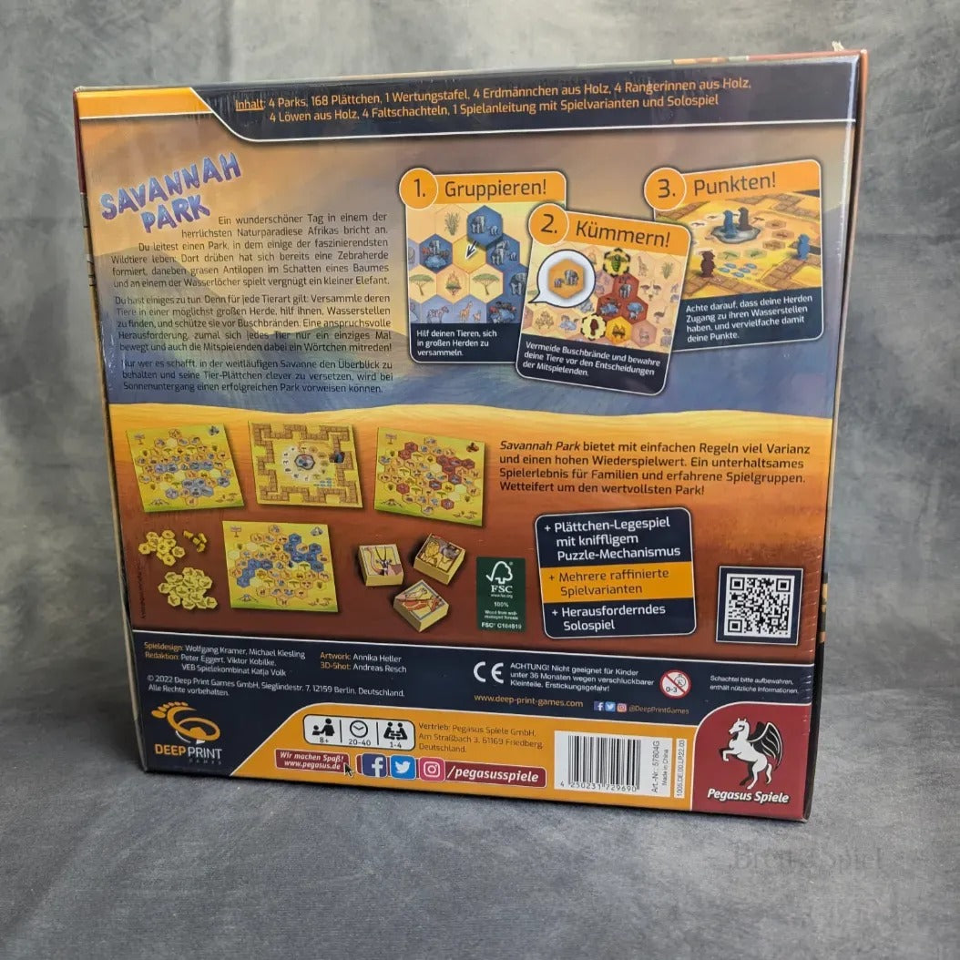 Die Rückseite der Schachtel Savannah Park von Pegasus Spiele zeigt eine deutsche Spielanleitung, illustrierte Beispiele dieses interaktiven Puzzles, bunte Bilder der größten Landtiere Afrikas, Komponenten, Logos und mehr.