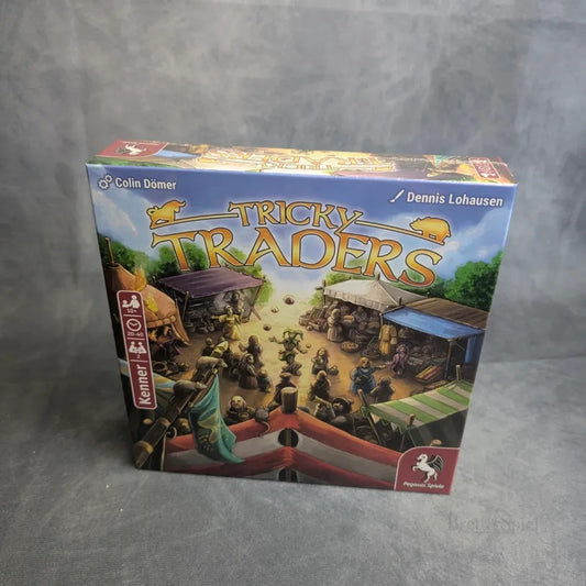 Die Tricky Traders Box von Pegasus Spiele zeigt eine bunte Marktszene mit Händlern, Zelten und Waren, den Titel in fettem Gelb und die Schöpfer Colin Dömer & Dennis Lohausen vermerkt. Es ist ein wahres Duellspiel der cleveren Handelsgilden!.