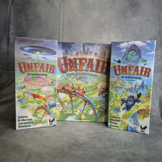 Drei Schachteln von Unfair - Fiese Freizeitparks inkl.. Erweiterungen "ABJW" + "CHKO" von Corax Games stehen aufrecht vor einem grauen Hintergrund, wobei die Hauptspielschachtel von den beiden Erweiterungsschachteln flankiert wird.