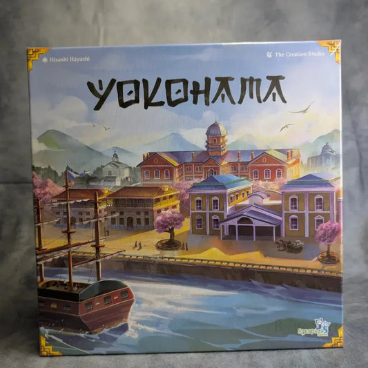 Das Cover des strategischen Brettspiels Yokohama von Synapses Games zeigt eine illustrierte japanische Hafenlandschaft mit traditionellen Gebäuden, rosa Bäumen und einem Holzschiff. Der Titel "Yokohama" steht oben prominent.