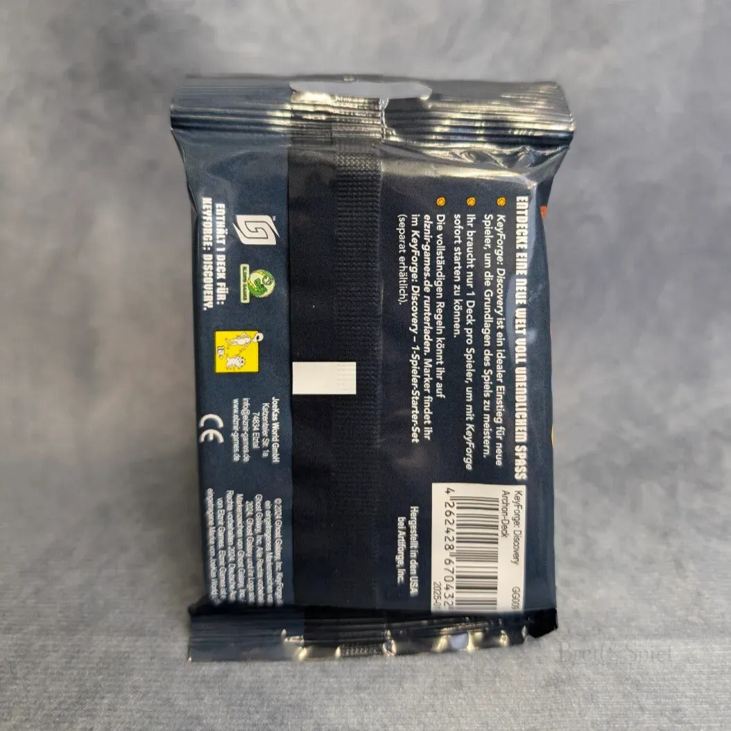 Eine versiegelte Packung KeyForge: Discovery Sammelkarten von JoeKas World GmbH von hinten gesehen, mit Barcode, Produktinfo und Symbolen auf dunkelblauem Hintergrund. Ideal für Einsteiger-Spiel und Fans von einzigartigen Decks. Liegt auf hellgrauer Oberfläche auf.