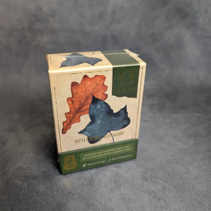 13 Leaves von JoeKas World GmbH: ein kompaktes deutsches Taktikspiel. Die beigefarbene Box zeigt ein Eichenblatt und eine Vogelsilhouette mit grünen Akzenten.