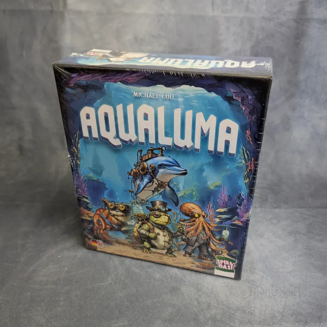 Eine Schachtel von Spiel Das! Aqualuma, ein kooperatives Brettspiel mit Unterwasserkreaturen - Delfin mit Taucher, Krabben, Schildkröten in Tauchausrüstung - vor einer farbenfrohen Kulisse für spannende Unterwasserabenteuer.