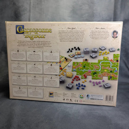 Die Rückseite der Carcassonne Big Box 3.1 von Hans im Glück zeigt den Titel des Spiels, die Beschreibung, die enthaltenen Erweiterungen, ein Foto des Aufbaus mit Plättchen und Figuren sowie Symbole für Spielerzahl und Altersempfehlung.