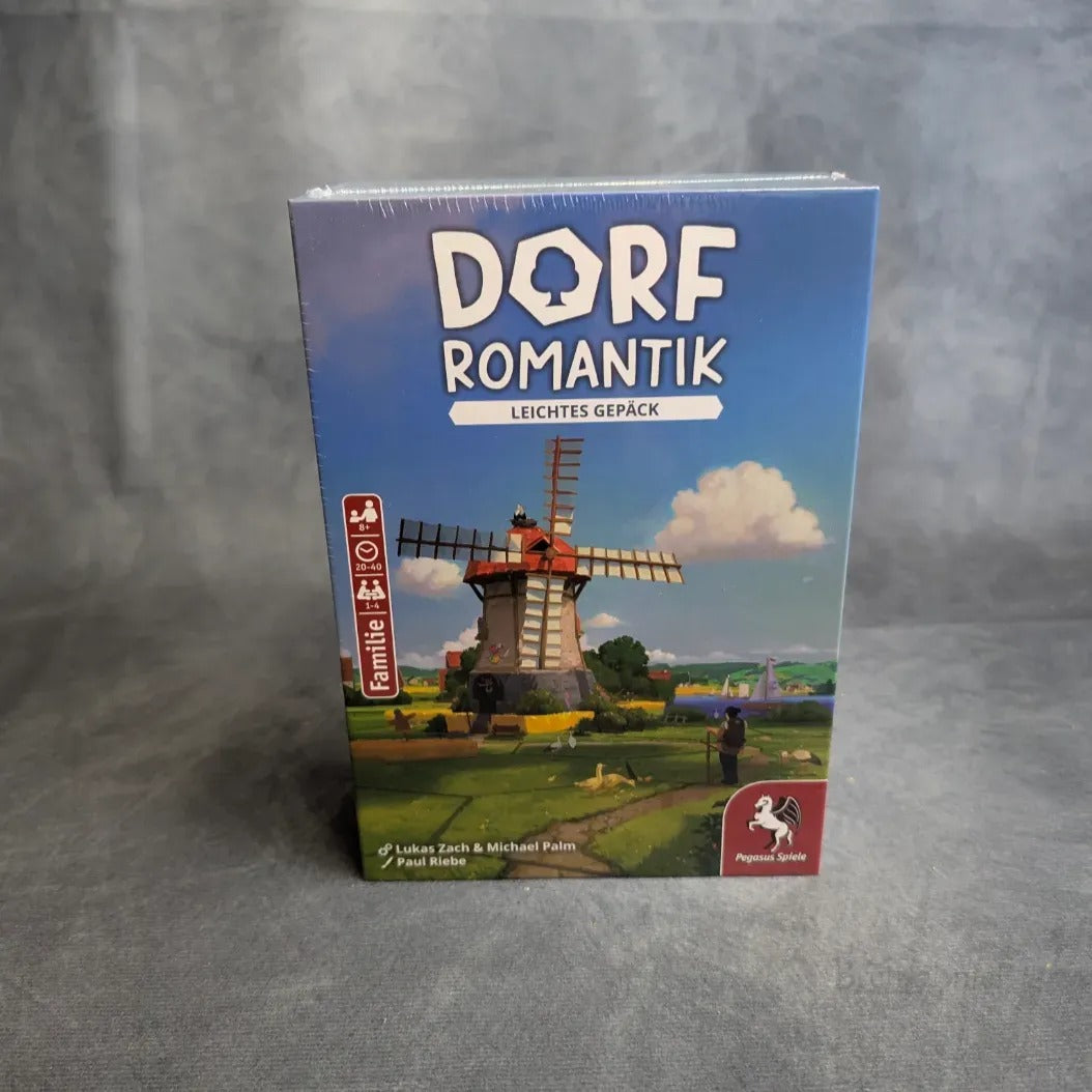 Eine Schachtel Dorfromantik: Leichtes Gepäck von Pegasus Spiele steht aufrecht auf einer grauen Fläche und zeigt ein Cover mit einer Windmühle, Bäumen und Feldern unter einem blauen Himmel mit Wolken.