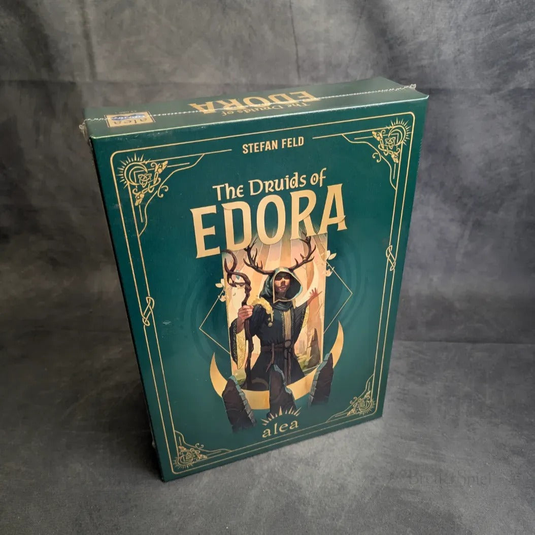 Aufrecht steht eine grüne Schachtel von Die Druiden von Edora von Pegasus Spiele. Das Keltenwald-inspirierte Cover zeigt einen geweihten Druiden mit Stab inmitten goldener Muster - ein magisches Strategiespiel für Abenteurer.