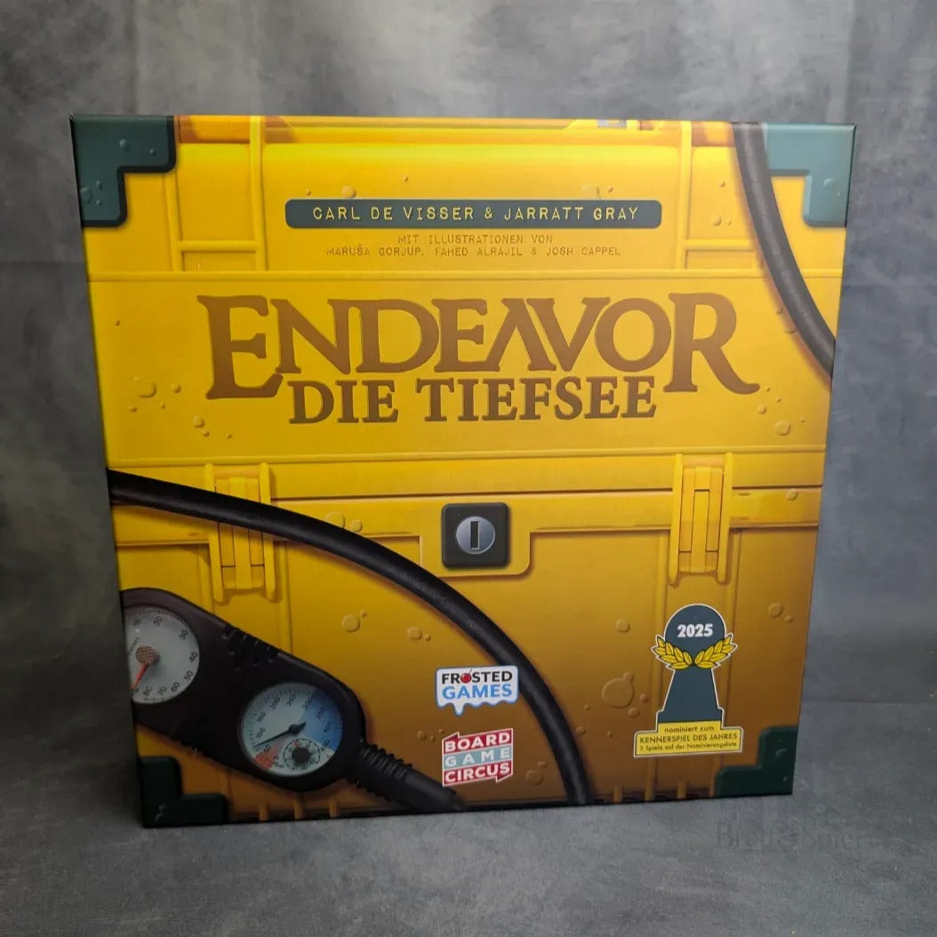 Ein Foto der Endeavor: Die Tiefsee-Box von Frosted Games, die ein gelbes Unterwassermotiv mit Manometer, Rohren, Nieten, Preissymbolen, darunter Kennerspiel des Jahres 2025, und Verlagslogos zeigt.