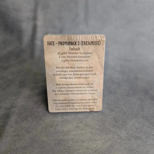Eine Fate: Die Verteidiger von Grimheim + Helden Erweiterung Sindra & Finkel + Promo Packs Karte von Elznier Games steht aufrecht auf grauem Stoff, mit abgenutzten Kanten und deutscher Anleitung - ideal für Brettspiel Fans.