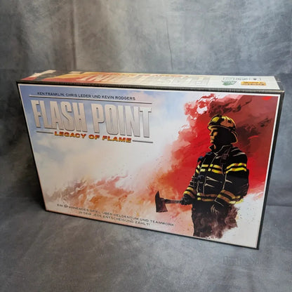 Das Flash Point Legacy: Deutsche Ausgabe von Heidelbär Games zeigt einen Feuerwehrmann mit einer Axt inmitten von Rauch und Flammen, mit den Namen der Schöpfer am oberen Rand der Schachtel.