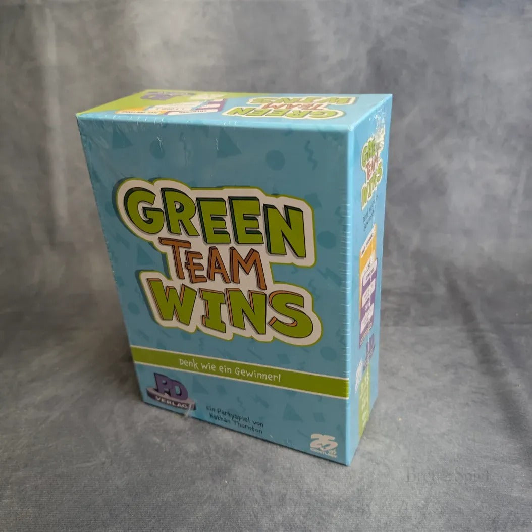 Eine versiegelte Schachtel der Green Teams Win des PD Verlags steht aufrecht auf einer grauen Fläche, mit buntem Schriftzug auf hellblauem Hintergrund und dem deutschen Slogan "Denk wie ein Gewinner!.