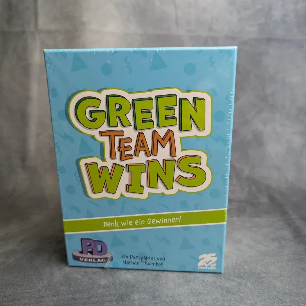 Eine blaue Schachtel der Green Teams Win des PD Verlags steht aufrecht auf einer grauen Fläche. Auf der Vorderseite befindet sich ein großer grüner und oranger Text, darunter ein kleinerer deutscher Text.