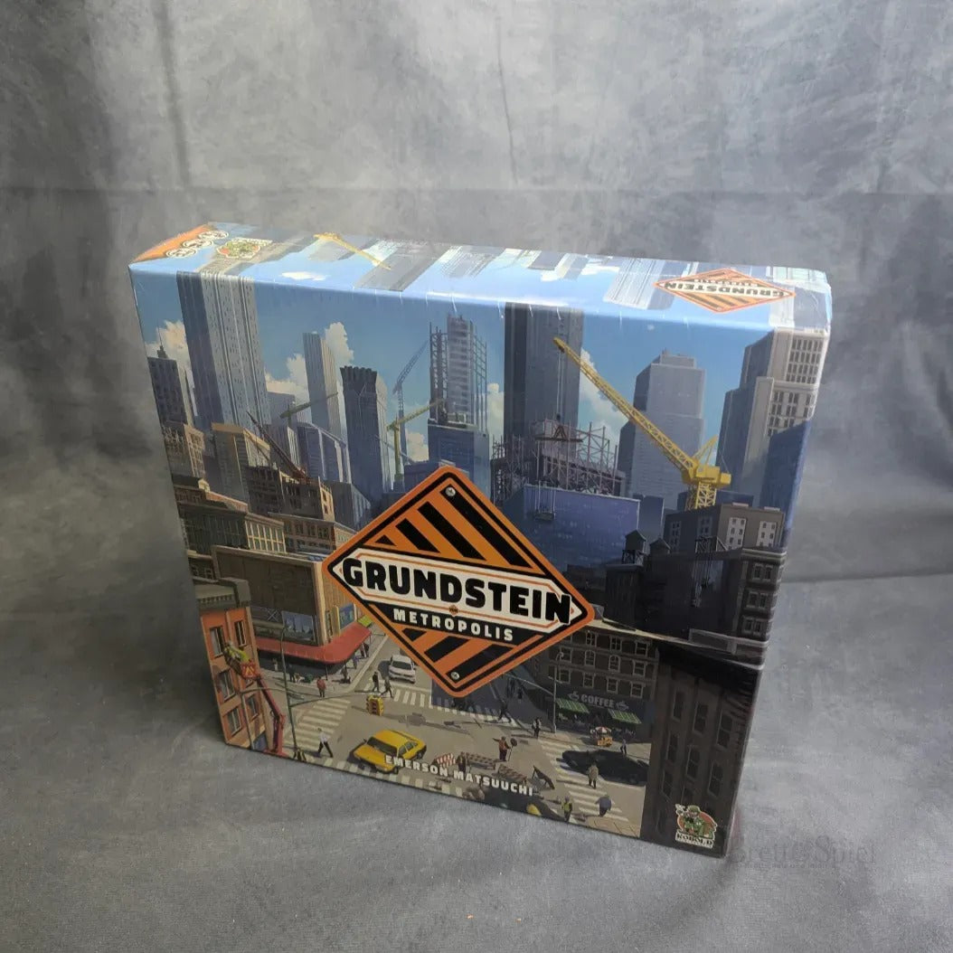 Eine eingeschweißte Schachtel von Grundstein von Metropolis von Kobold Spiele zeigt eine illustrierte Stadtlandschaft mit hohen Gebäuden und Kränen auf grauem Hintergrund, die das faszinierende Polyomino-Spielprinzip widerspiegelt.