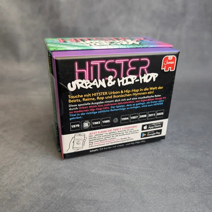 Eine Schachtel Hitster - Urban & Hip-Hop von Jumbo Spiele ruht auf einem grauen Hintergrund, mit buntem, fettgedrucktem Text und deutschen Partyspiel-Details, einer Zeitleiste der Jahre und dem roten Jumbo Spiele-Logo auf der Verpackung.