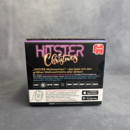 Eine schwarze Schachtel mit der Aufschrift Hitster: Christmas von Jumbo Spiele ist mit Neonschriftzügen, einem deutschen Text über eine Weihnachtslieder Musik-Challenge, einer Zeitleiste und den Logos von App Store und Google Play am unteren Rand versehen.