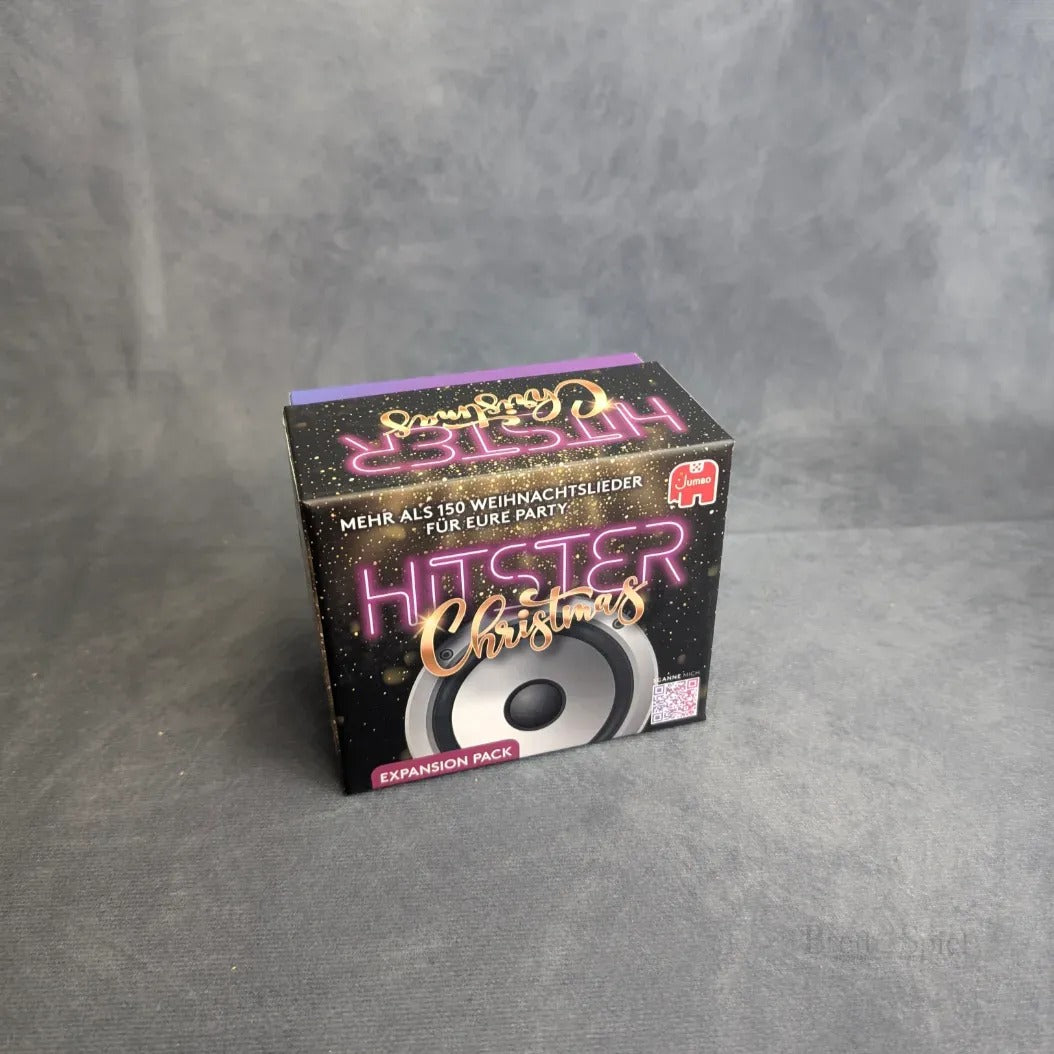 Eine schwarze Box mit der Aufschrift Hitster: Christmas von Jumbo Spiele mit dem Neon-Text "Weihnachten" und "Expansion Pack" steht auf einer grauen Fläche und hebt eine Musik-Challenge mit über 150 Weihnachtsliedern und einer Lautsprechergrafik hervor.