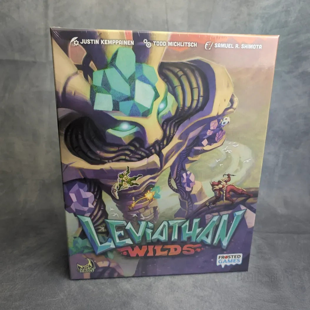 Die Leviathan Wilds-Box von Frosted Games zeigt eine lebendige, gepanzerte Kreatur mit leuchtenden Augen, die von kleinen Abenteurern in diesem kooperativen Spiel erklommen und bekämpft wird. Oben auf der Schachtel sind die Credits der Designer zu sehen.