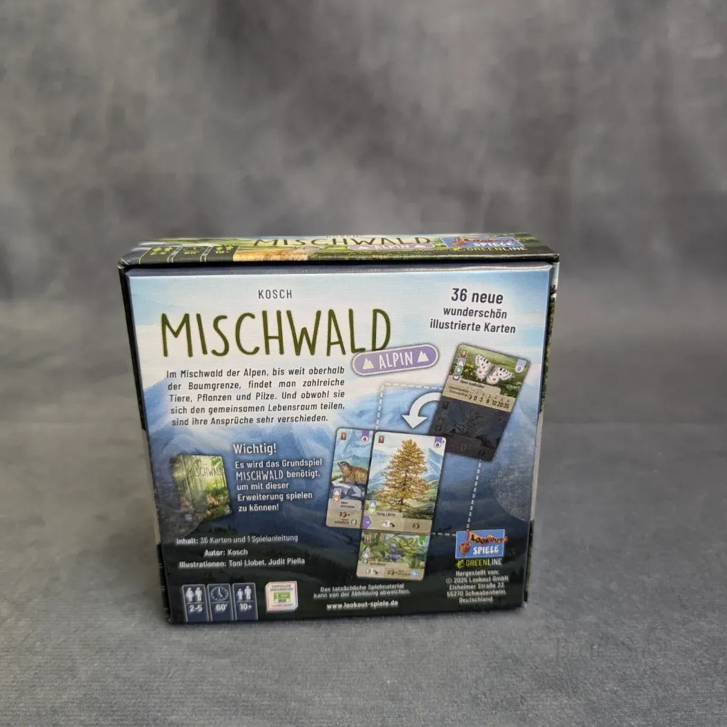 Eine Schachtel von Asmodee's Mischwald - Alpin steht vor einem grauen Hintergrund, der Illustrationen der Alpenflora und -fauna zeigt. Der deutsche Text beschreibt das Spiel, das 36 neue illustrierte Karten mit Bäumen, Tieren und Pflanzen enthält.