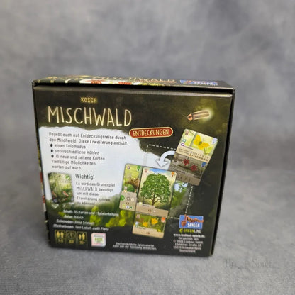 Eine Schachtel für Brett&Spiels Mischwald - Entdeckungen steht auf einer grauen Fläche. Die Rückseite zeigt bunte Kartenillustrationen, deutsche Spielinformationen und Icons, die die Komponenten dieser taktischen Kartenspielerweiterung hervorheben.