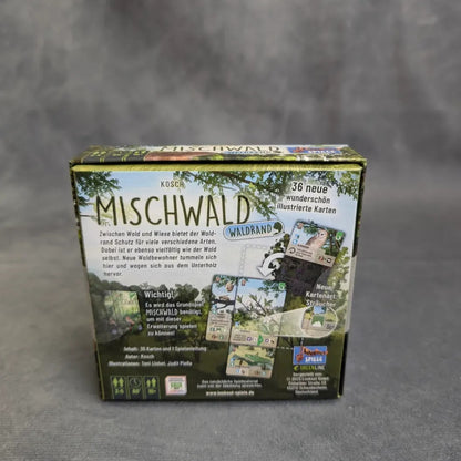 Eine Schachtel von Asmodee's Mischwald - Waldrand ruht auf einer grauen Oberfläche. Die Rückseite zeigt deutschen Text, lebendig illustrierte Karten und Bilder, die die Komponenten und Details des Spiels zeigen.
