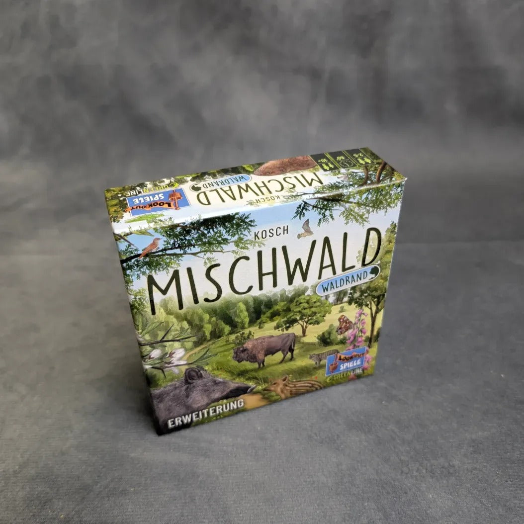 Eine Schachtel von Asmodee's Mischwald - Waldrand, mit illustrierten Waldtieren und Landschaften auf dem Deckel, ruht auf einer grauen Fläche.