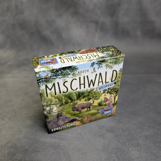 Eine Schachtel von Asmodee's Mischwald - Waldrand, mit illustrierten Waldtieren und Landschaften auf dem Deckel, ruht auf einer grauen Fläche.