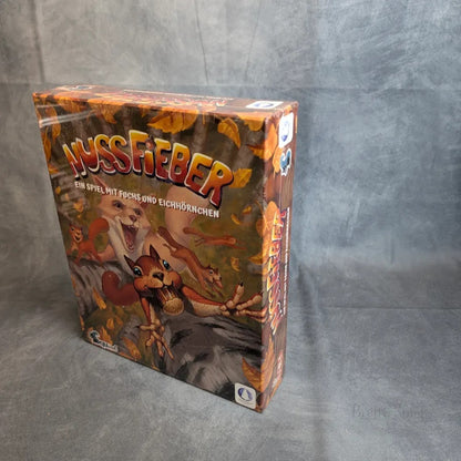 Die Spielschachtel Nussfieber der Squink GmbH ist eingeschweißt und zeigt auf dem Cover illustrierte Eichhörnchen und einen Fuchs, die nach herabfallenden Nüssen greifen, vor einem grau strukturierten Hintergrund.