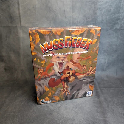 Nussfieber von Squink GmbH zeigt eine Eichhörnchenbande und einen schlauen Fuchs zwischen Herbstblättern. Der Untertitel der Schachtel lautet: Ein Spiel mit Fuchs und Eichhörnchen.