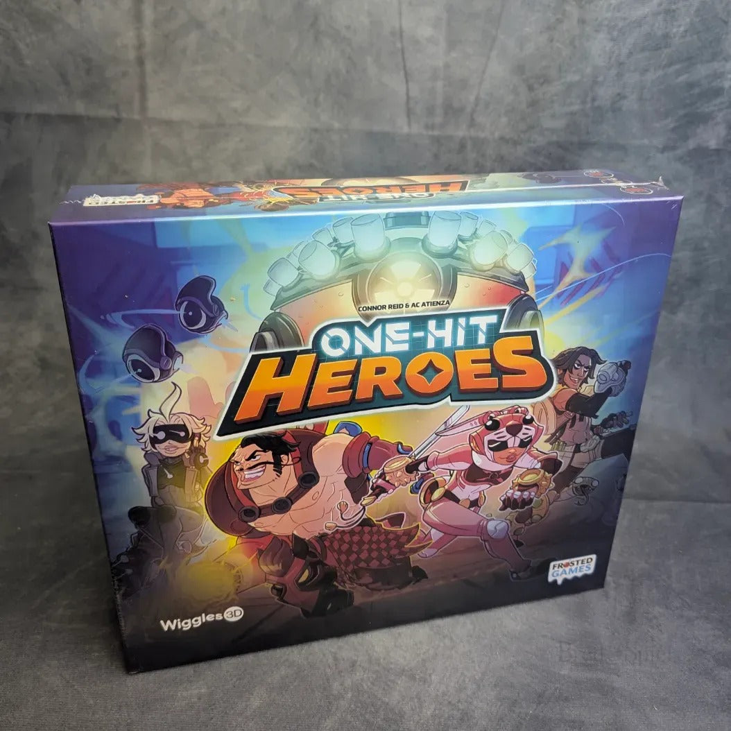 Die farbenfrohe Schachtel von One Hit Heroes von Frosted Games zeigt animierte Charaktere - Ritter, Roboter und rosahaarige Kämpfer - in Action-Posen, die die Spannung dieses kooperativen Kartenspiels im klassischen Boss-Rush-Stil widerspiegeln.