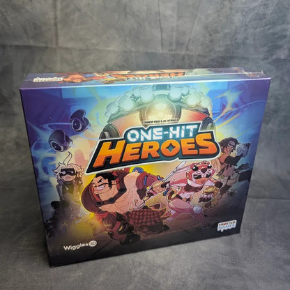 Die farbenfrohe Schachtel von One Hit Heroes von Frosted Games zeigt animierte Charaktere - Ritter, Roboter und rosahaarige Kämpfer - in Action-Posen, die die Spannung dieses kooperativen Kartenspiels im klassischen Boss-Rush-Stil widerspiegeln.