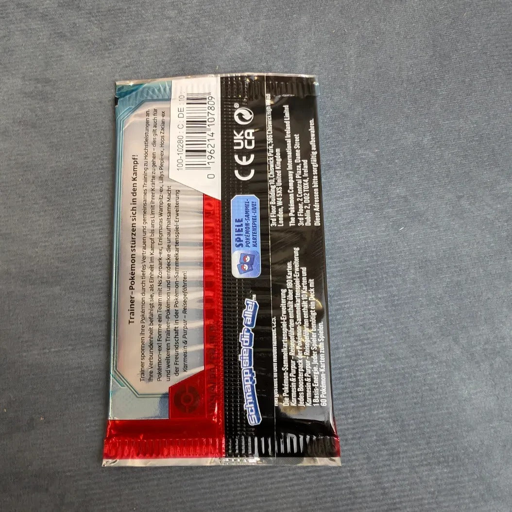 Ein versiegelter Pokèmon PKM KP09 Reisegefährten Booster von Burst Spiele liegt mit der Vorderseite nach unten auf einer grauen Fläche und zeigt die Rückseite mit einem Barcode, Produktdetails und einem deutschen Branding.