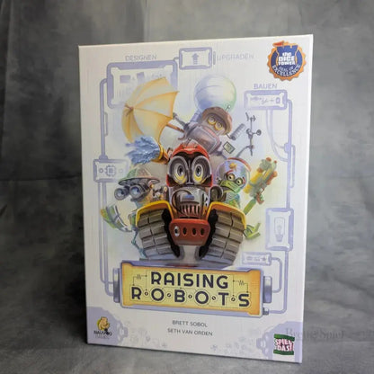 Das Cover des Brettspiels Raising Robots zeigt einladende Illustration von buunten Robotern mit vielen Gimmicks. Es deutet auf ein Familienfreundliches Spiel oder strategisches Aufbauspiel hin, bei dem es darum geht den besten Roboter zu bauen 