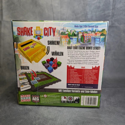Die Rückseite der Schachtel von Shake That City von Boardgame Circus zeigt die bunten Spielsteine, die Schüttelvorrichtung, die Spieldetails und die Funktionen. Anleitungen, Altersangaben und Spielerinformationen befinden sich am unteren Rand der Verpackung dieses taktischen Brettspiels.