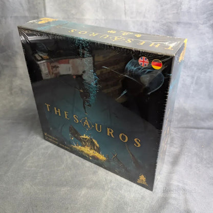 Ein eingeschweißtes Thesauros-Brettspiel von JoeKas World GmbH mit dunkler Grafik mit goldenen Akzenten, einem Taucher, einer Schatztruhe, Münzen und deutschen/britischen Flaggen als Sprachoptionen. Die Schachtel ist auf einer grauen Oberfläche abgebildet.