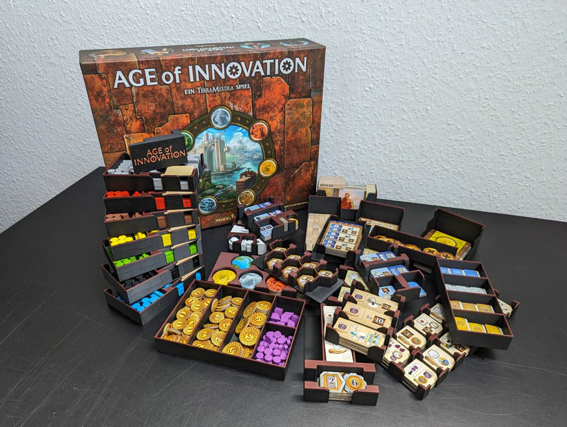 Das Age of Innovation Insert von 3D-Inset zeigt, wie bunte Spielsteine, Kacheln, Karten und Holzteile ordentlich in Fächern auf einer schwarzen Oberfläche angeordnet werden, wobei die Spielschachtel im Hintergrund sichtbar ist.