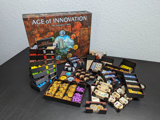 Das Age of Innovation Insert von 3D-Inset zeigt, wie bunte Spielsteine, Kacheln, Karten und Holzteile ordentlich in Fächern auf einer schwarzen Oberfläche angeordnet werden, wobei die Spielschachtel im Hintergrund sichtbar ist.