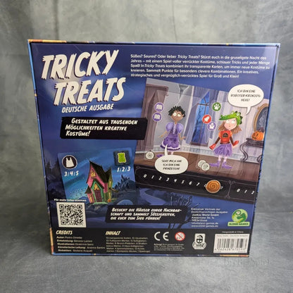 Die Rückseite der Tricky Treats-Schachtel von JoeKas World GmbH zeigt verkleidete Zeichentrick-Kinder in einem gruseligen Haus mit Spielsteinen, deutschem Text zu diesem lustigen Halloween-Familienspiel, Symbolen und einem QR-Code.
