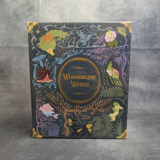 Eine Schachtel von Strohmann Spiele mit der Aufschrift "Wundersame Wesen + Besatzungs-Set + Gigantische Bestien Erweiterung" zeigt farbenfrohe Illustrationen von fantastischen Kreaturen, Fantasiepflanzen und Pilzen auf dunklem Hintergrund.