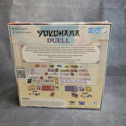 Rückseite der Yokohama: Duell-Box von Synapses Games mit Spielmaterial, Aufbaufotos und deutscher Beschreibung - strategisches Handelsspiel aus der Meiji-Ära. Logos und Credits oben/unten, Box auf grauer Fläche.