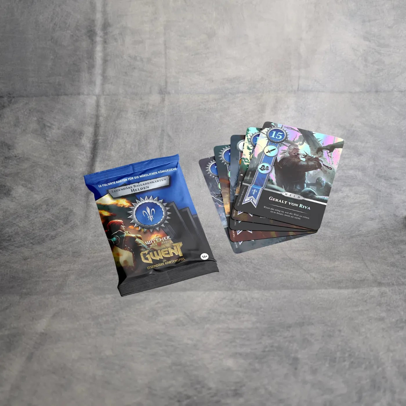 Ein versiegeltes Gwent - Legendäre Balladenkarten-Paket von Asmodee liegt auf einer grauen Fläche neben einem aufgefächerten Satz von fünf überlappenden Folien-Charakterkarten.