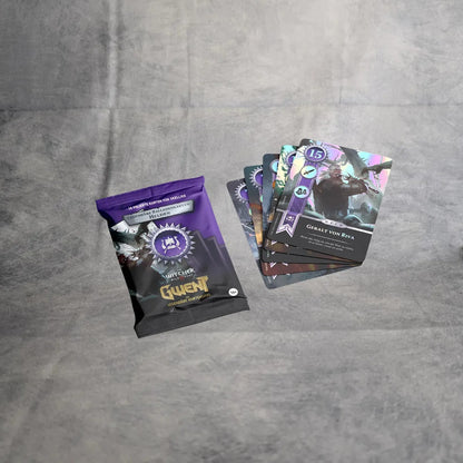 Eine versiegelte Asmodee Gwent - Legendäre Balladenkarten Packung ruht auf einer grauen Oberfläche neben fünf illustrierten Karten, wobei die oberste Karte Great Von Rivia aus dem The Witcher-Universum zeigt.