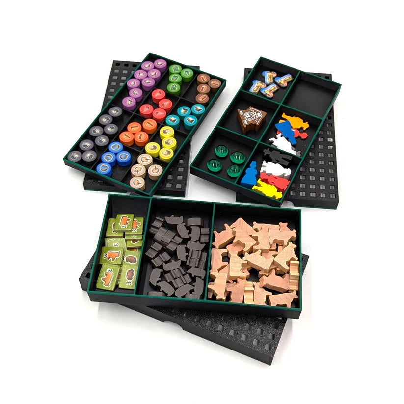 Drei offene schwarze Tabletts aus dem Black Forest Insert von 3D-Inset sind mit bunten Spielsteinen, hölzernen Tierfiguren und anderen Brettspielteilen gefüllt, die alle ordentlich auf einem weißen Hintergrund angeordnet sind.